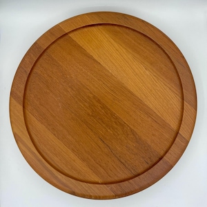 Puede incluir: Una bandeja redonda de madera para servir con un acabado de madera natural. La bandeja tiene un borde elevado y es perfecta para servir queso, galletas o aperitivos.