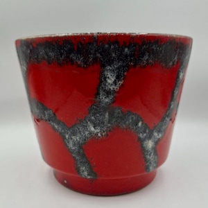 Puede incluir: Jardinera de cerámica roja con un diseño abstracto en blanco y negro. La jardinera tiene forma acampanada y una base pequeña. El borde de la jardinera tiene un ribete dorado metálico. Adecuada para uso en interiores o exteriores. Mide unos 15 cm de altura.