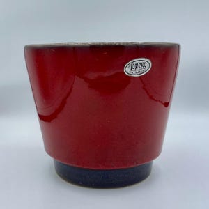 Op de afbeelding: Rode keramische plantenpot met een donkerblauwe rand en een wit label met de tekst "Topeko Keramik".
