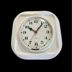 Puede incluir: Reloj de cuarzo color crema con marco cuadrado y acanalado. La esfera del reloj es blanca con números negros, un borde dorado y un segundero rojo. El texto "QUARTZ" está impreso en la esfera. El reloj marca la 1:07.