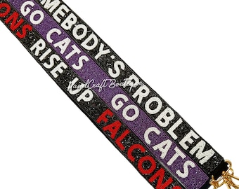 Pode incluir: Uma alça de contas com as palavras "Somebody's Problem", "Go Cats" e "Falcons Rise Up" em letras brancas e vermelhas sobre um fundo preto.