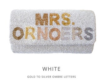 Könnte beinhalten: Weiße Perlenclutch mit "MRS. ORNOERS" in gold-silbernem Farbverlauf.