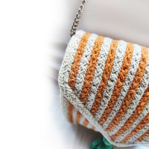 Op de afbeelding: Een gehaakte tas met oranje en witte strepen en een zilveren kettingband.