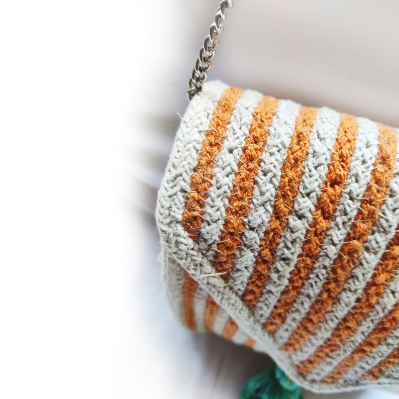 Op de afbeelding: Een gehaakte tas met oranje en witte strepen en een zilveren kettingband.