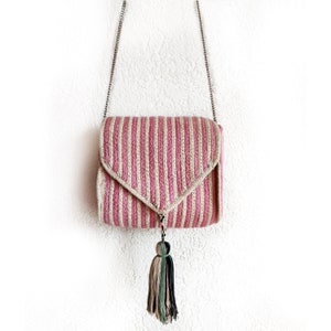 Op de afbeelding: Een roze en beige gestreepte gehaakte schoudertas met een kwast. De tas heeft een zilveren kettingband.