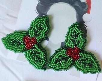 May include: A pair of green and red beaded holly leaf earrings. The leaves are made of green beads and the berries are made of red beads.