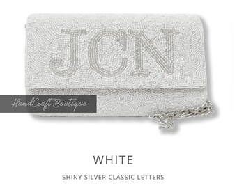 May include: White beaded clutch with a silver chain strap and the letters "JCN" in shiny silver.