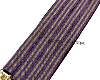 May include: Purple and gold striped beaded trim with a gold metal clasp. HANDCRAFT BOUTIQUE is printed on the trim.