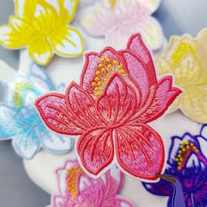 Puede incluir: Parches bordados de flores de loto en varios colores, incluyendo rojo, amarillo, rosa, azul y morado. Cada parche presenta costuras detalladas y un borde blanco. Los parches son probablemente para fines decorativos, como ropa o accesorios.