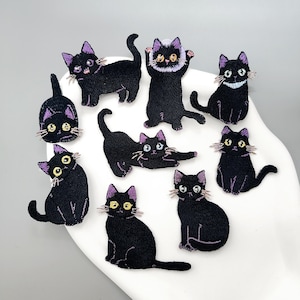 May include: A collection of eight embroidered black cat patches featuring various poses. Each cat has purple-accented ears, yellow or white eyes, and detailed stitching. The patches are arranged in a group, showcasing different feline expressions and postures.