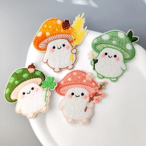 May include: Four embroidered patches featuring white mushroom-shaped characters with smiling faces and rosy cheeks. One holds yellow wheat, one a white flower, one a green clover, and one a pink flowering branch. Each has a colorful spotted cap.