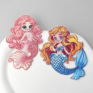 May include: Two embroidered patches featuring cartoon mermaids. One mermaid has long pink hair and a pink tail with a light pink bodice. The other mermaid has long golden-yellow hair, a blue tail, and a blue bodice. Both have large blue eyes.
