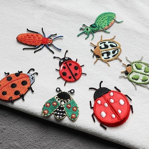 Könnte beinhalten: Eine Sammlung gestickter Insektenaufnäher, darunter Marienkäfer, Käfer und eine Spinne. Die Aufnäher weisen leuchtende Farben wie Rot, Orange, Grün und Braun mit detaillierten Nähten auf. Ideal zum Dekorieren von Kleidung oder Accessoires.