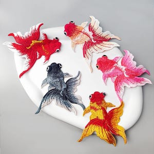 Puede incluir: Parches bordados de peces dorados en rojo, rosa, amarillo y azul. Los parches presentan costuras detalladas y están dispuestos sobre una superficie blanca. Estos parches decorativos son ideales para añadir un toque único a la ropa o los accesorios.