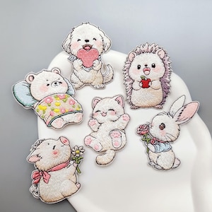 May include: Embroidered patches featuring adorable animal designs. Includes a dog holding a heart, a bear in bed, a cat, a hedgehog with an apple, a pig with a flower, and a bunny with a rose. Each patch has detailed stitching and vibrant colors.