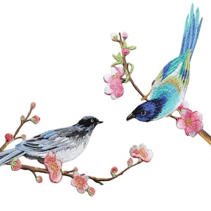 Puede incluir: Parches bordados con dos pájaros coloridos posados en ramas florecidas. Uno tiene plumas azules, verdes y amarillas, el otro es gris y blanco. Flores rosas y ramas marrones completan el diseño.