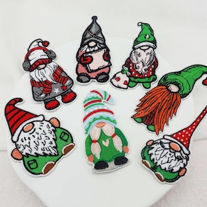 Puede incluir: Una colección de parches bordados de gnomos. Cada parche presenta un gnomo con una larga barba y un gorro puntiagudo. Los gnomos visten varios atuendos en rojo, verde y gris, con barbas y detalles blancos.