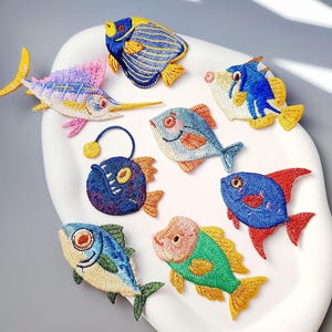 Può includere: Una collezione di toppe di pesci ricamati in vari colori, tra cui blu, giallo, rosso e verde. Le toppe presentano cuciture dettagliate e raffigurano diverse specie di pesci, perfette per aggiungere a vestiti o accessori.
