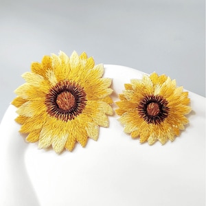 Peut inclure: Deux écussons brodés en forme de tournesol avec des pétales jaune vif et un centre brun foncé. Les écussons sont circulaires avec des coutures détaillées qui imitent la texture des pétales de fleurs naturelles, présentant une version plus grande et une plus petite.