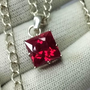 Peut inclure: Un collier en argent avec un pendentif en forme de carré orné d'une grande pierre rouge foncé.