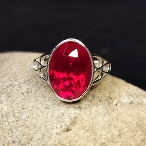 May include: A silver ring with a large, oval-shaped ruby gemstone. The ring has a delicate, openwork design.