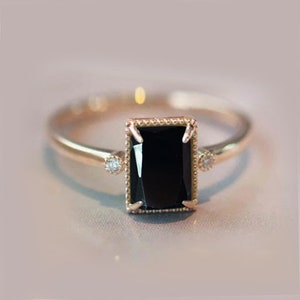 May include: A gold ring with a black rectangular gemstone and two smaller clear gemstones on the band.