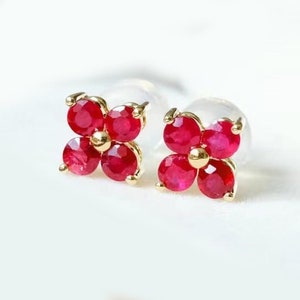 Op de afbeelding: Een paar gouden oorbellen met vier rode robijnstenen die in de vorm van een bloem zijn gezet.