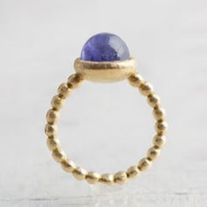 May include: A gold ring with a beaded band and a round, purple gemstone.