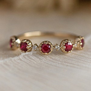 Op de afbeelding: Een gouden ring met vijf rode robijnstenen en kleine diamanten die tussen elke steen zijn gezet.