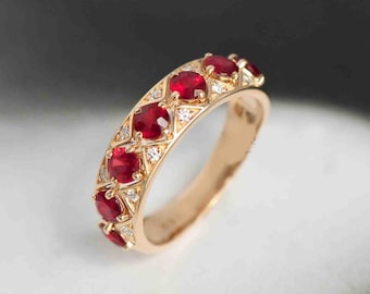Puede incluir: Un anillo de banda de oro con una fila de rubíes rojos y pequeños diamantes engastados en un patrón geométrico.