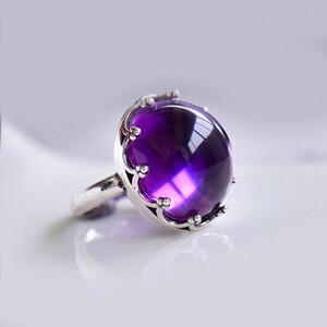 Puede incluir: Un anillo de plata con una gran amatista redonda y púrpura engastada en un engaste de corona adornado.
