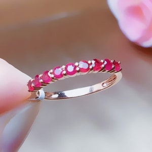May include: A delicate gold band ring with a row of small, bright red ruby stones.