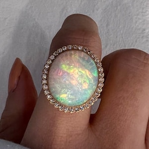 May include: A gold ring featuring a large oval opal gemstone set within a halo of small diamonds.