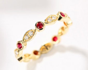 Puede incluir: Anillo de banda de oro con un diseño delicado que presenta piedras preciosas rojas y pequeñas piedras transparentes alternadas.