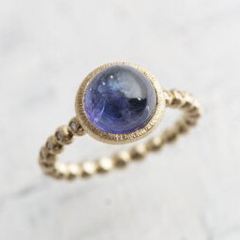 May include: A gold ring with a twisted band and a round, bezel-set blue gemstone.