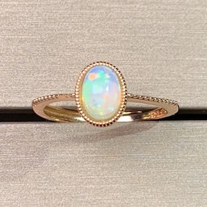 May include: A delicate gold ring with a white opal gemstone set in a bezel setting. The ring has a simple band with a beaded edge.