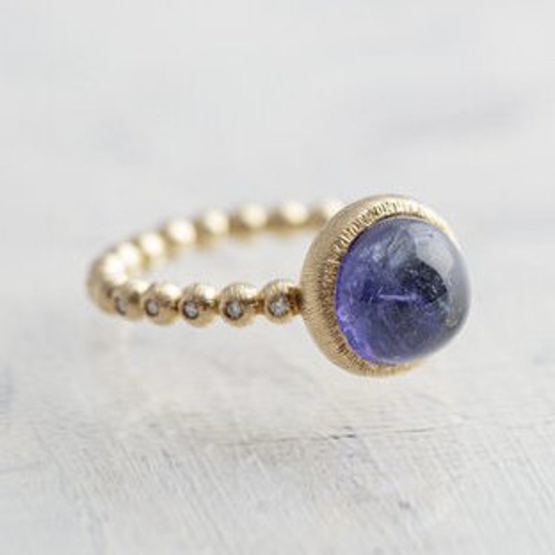 May include: A gold ring with a beaded band and a large, round, purple gemstone set in a textured gold setting.