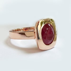 May include: A rose gold ring with a red ruby gemstone set in a square bezel.