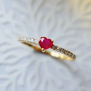 May include: A delicate gold ring with a small heart-shaped ruby gemstone and a band of tiny sparkling diamonds.