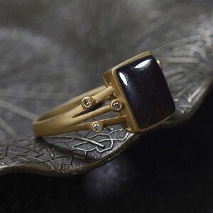May include: A gold ring with a dark blue gemstone and four small diamonds. The ring has a unique design with three gold bands that extend from the gemstone setting.