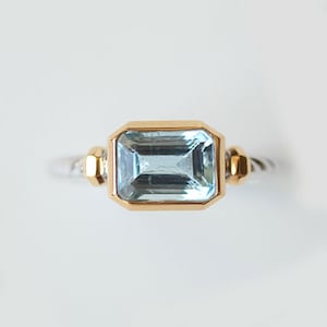 May include: A gold and silver ring with a light blue aquamarine gemstone.