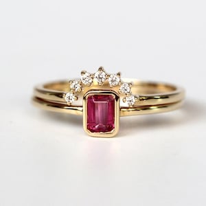 May include: A gold ring set with a pink emerald-cut gemstone and a row of small diamonds.