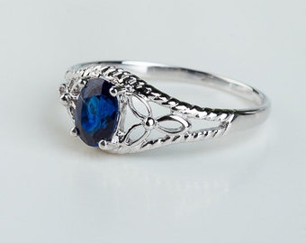 May include: A silver ring with a blue oval-shaped gemstone set in a delicate filigree design. The band is twisted and has a polished finish.