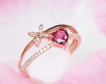May include: A rose gold ring with a heart-shaped pink gemstone and a delicate flower design. The ring is set with small diamonds.