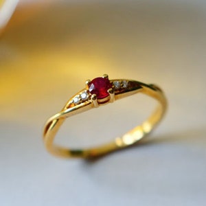 Può includere: Un delicato anello a fascia d'oro con un piccolo rubino rosso e tre diamanti più piccoli incastonati nella fascia.