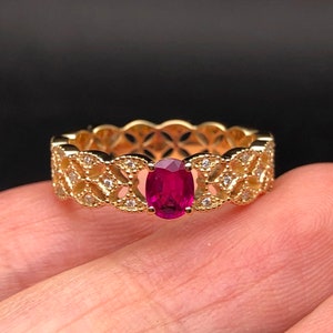 May include: A gold ring with a delicate filigree design and a bright red oval ruby gemstone.