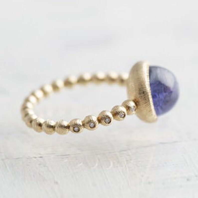 May include: A gold ring with a beaded band and a large, round, purple gemstone. The band is accented with small diamonds.