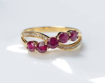 Puede incluir: Un anillo de oro con un diseño delicado e entrelazado presenta cinco piedras preciosas de rubí rojo y pequeños diamantes brillantes.