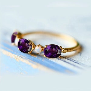 May include: A gold band ring with five oval-shaped gemstones. The ring features three purple amethysts and two white opals.