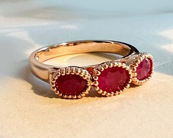 May include: A gold ring featuring three oval-shaped ruby gemstones set in a delicate, beaded design.